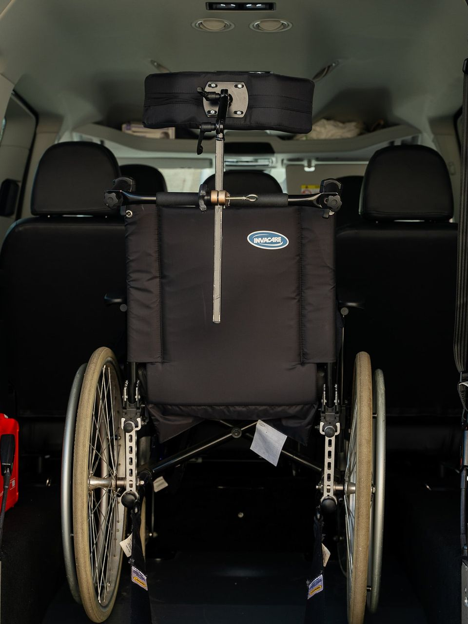 Un fauteuil roulant est fixé dans un véhicule, avec appuie-tête et siège noir, tourné dos au spectateur.