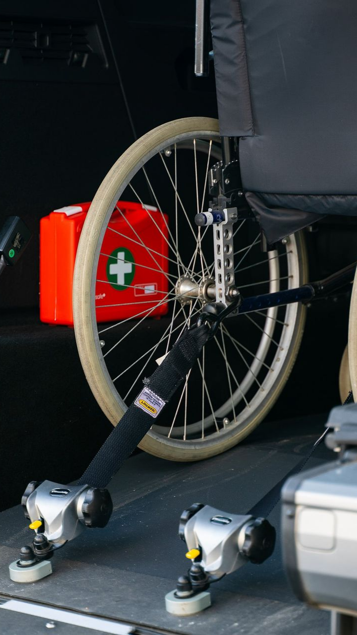 Fauteuil roulant fixé dans le véhicule à l'aide de sangles et de dispositifs de blocage des roues ; trousse de premiers secours en arrière-plan.