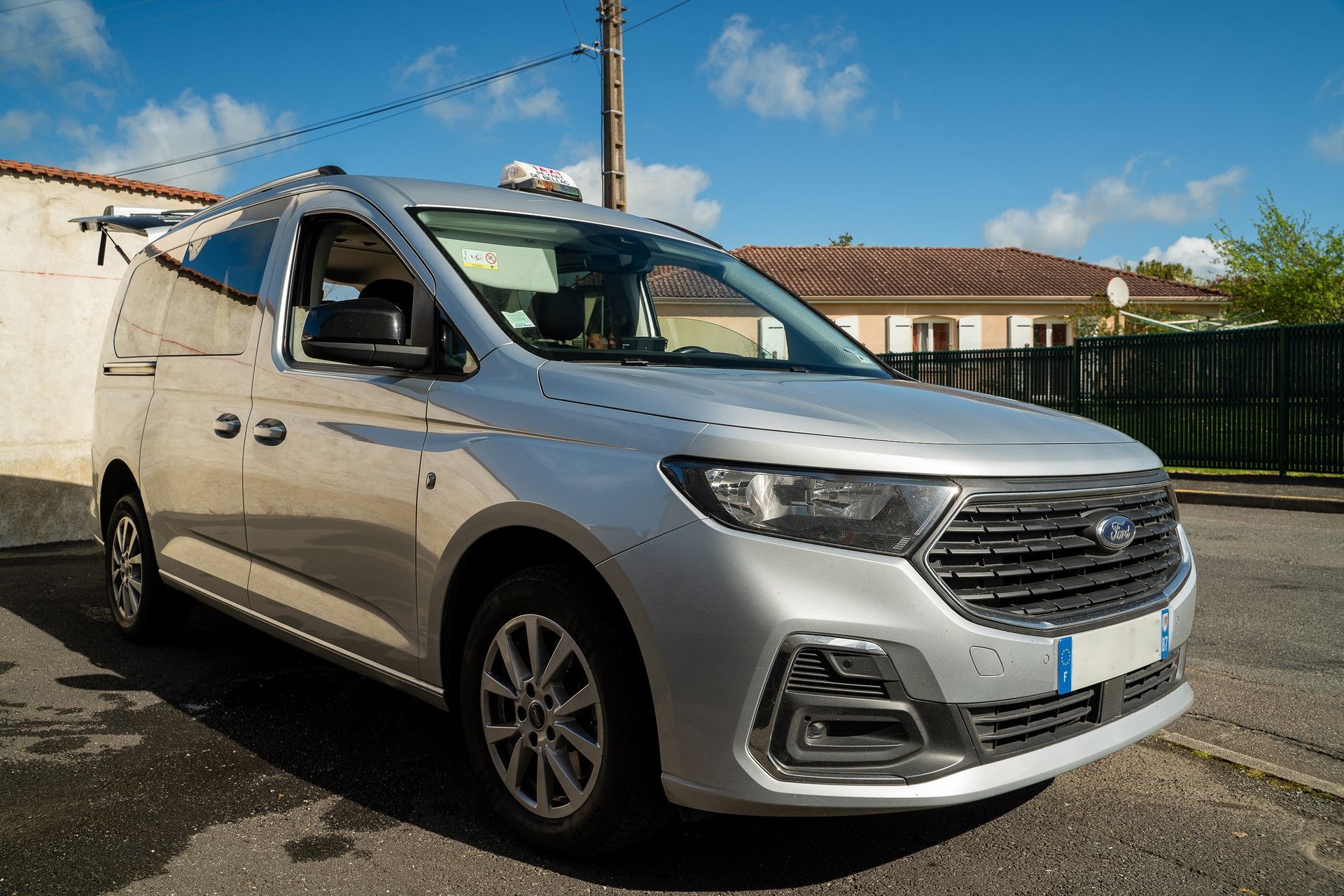 Fourgonnette Ford argentée garée dans la rue, devant une maison.