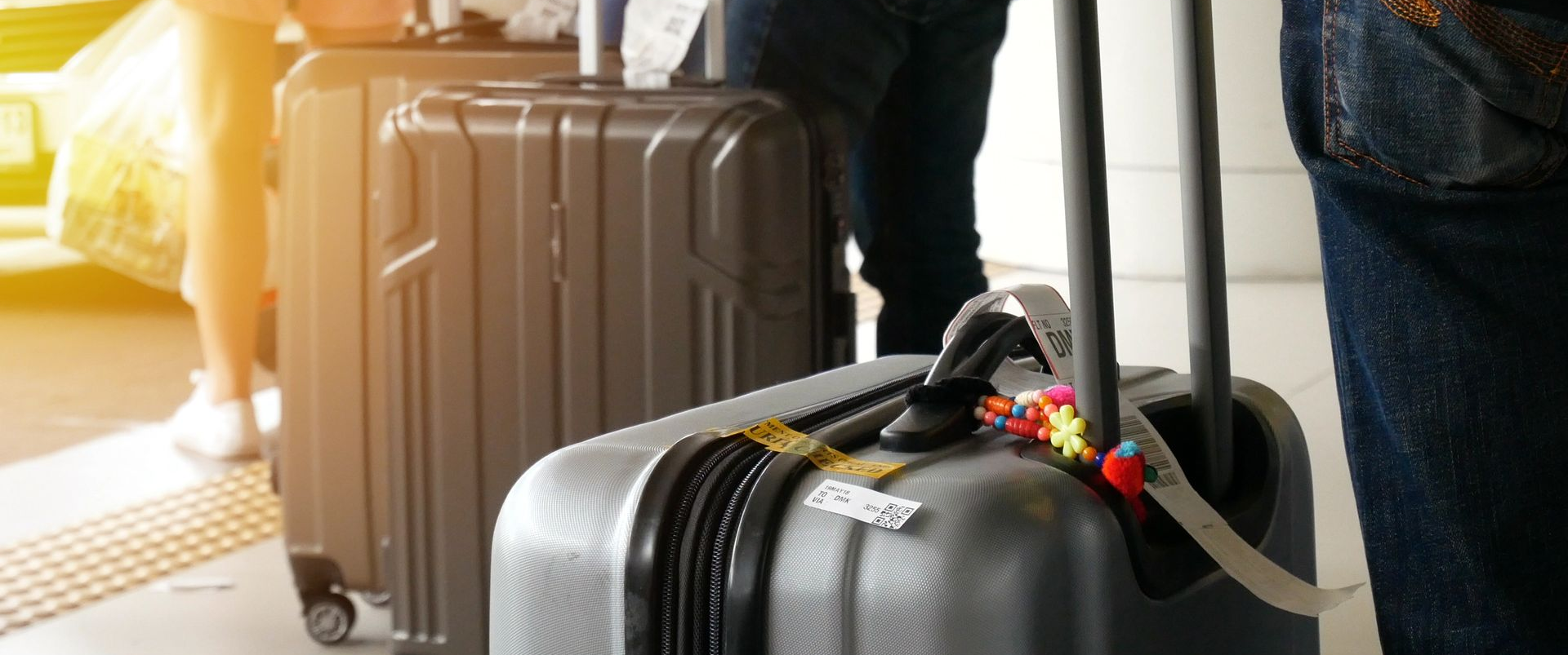 Valises avec étiquettes à bagages, tenues par des personnes, possiblement dans un aéroport ou une gare.