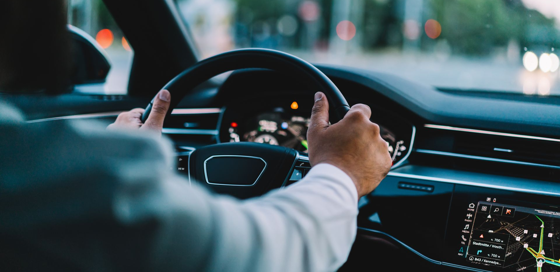 Mains sur le volant, conduite d'une voiture, arrière-plan flou avec des arbres verts et des lumières orange.
