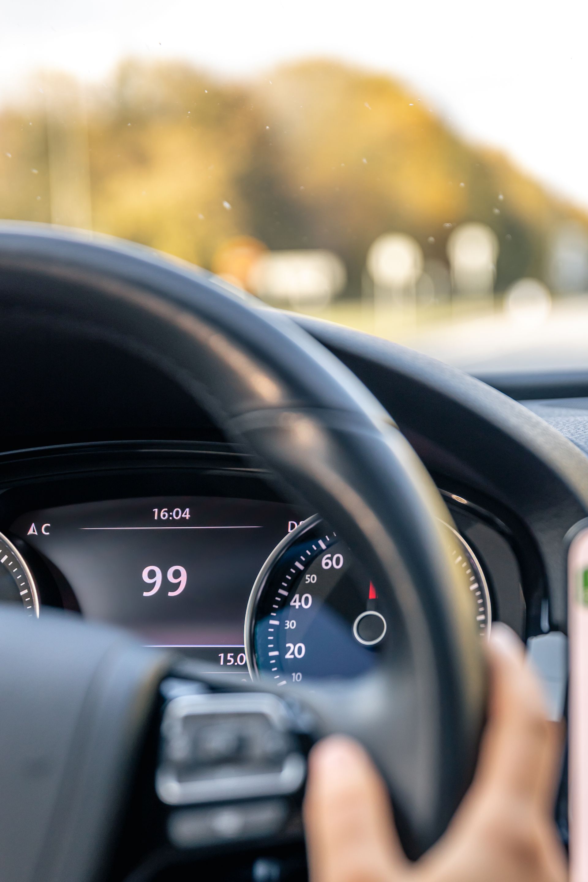Vue du tableau de bord en conduisant. Le compteur de vitesse indique 99 km/h. La main du conducteur serre le volant.