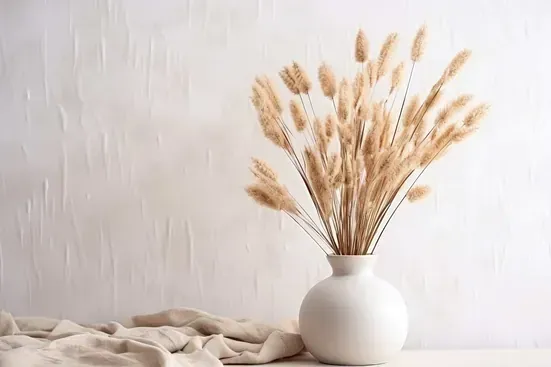 Un jarrón blanco lleno de flores secas sobre una mesa.