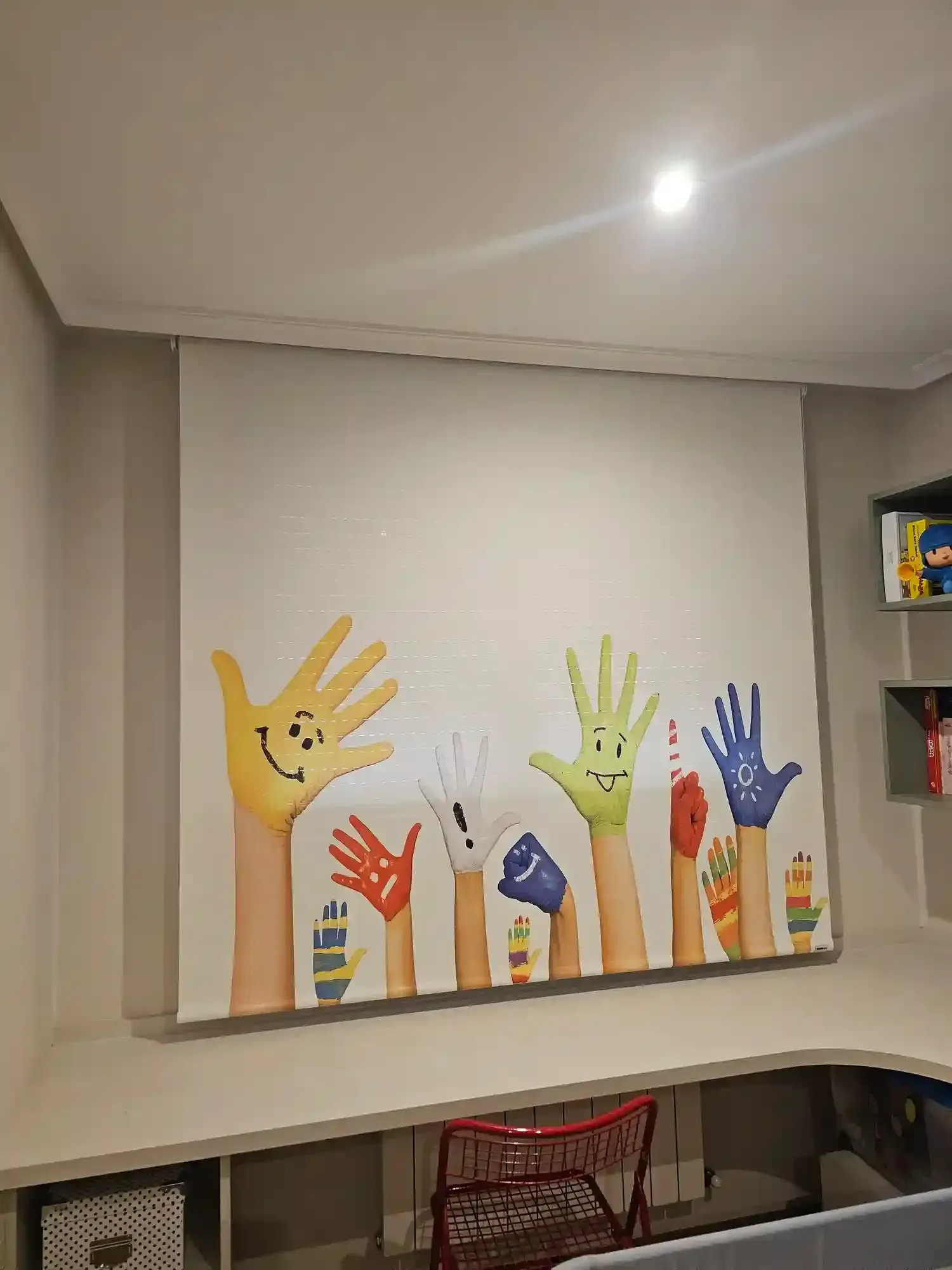 Mural colorido de huellas de manos en relieve en amarillo, naranja, verde y azul en una pared de una habitación.