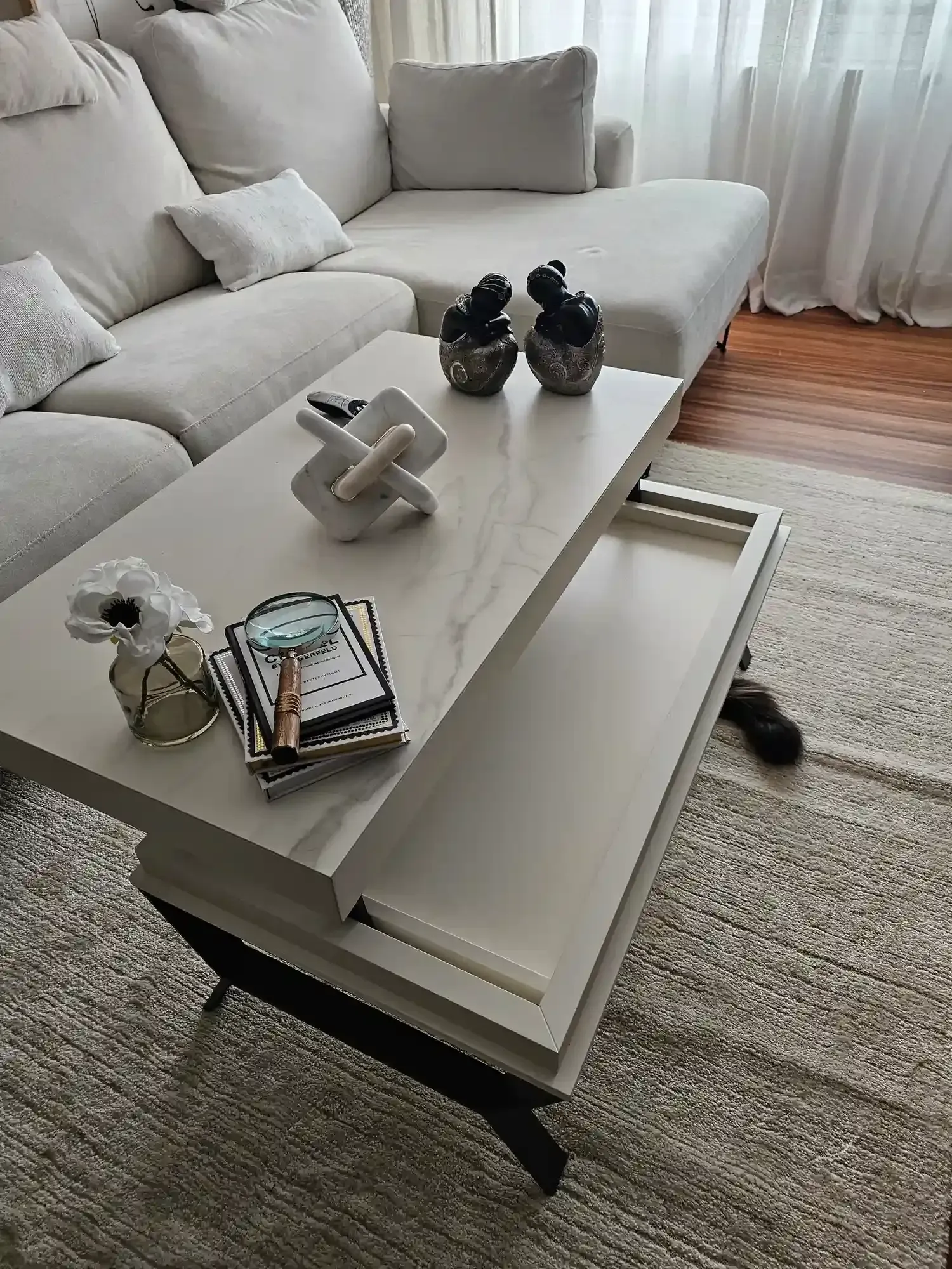 Sala de estar con sofá color crema y mesa de centro abierta con cajón para revistas y objetos decorativos.
