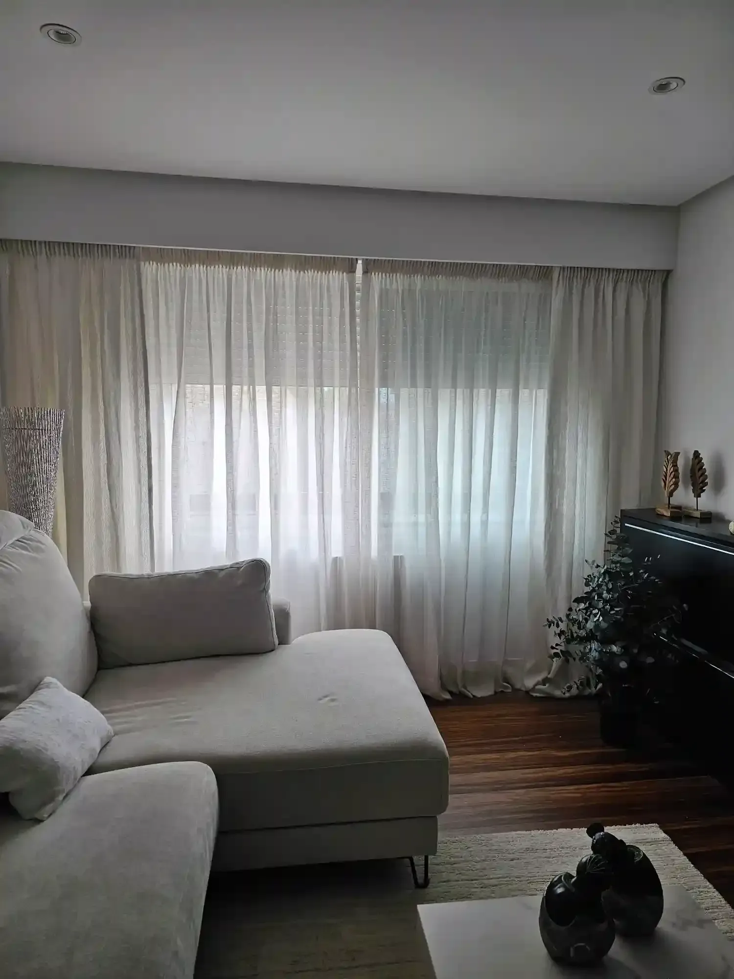 Sala de estar con un sofá modular gris, cortinas transparentes, suelo de madera