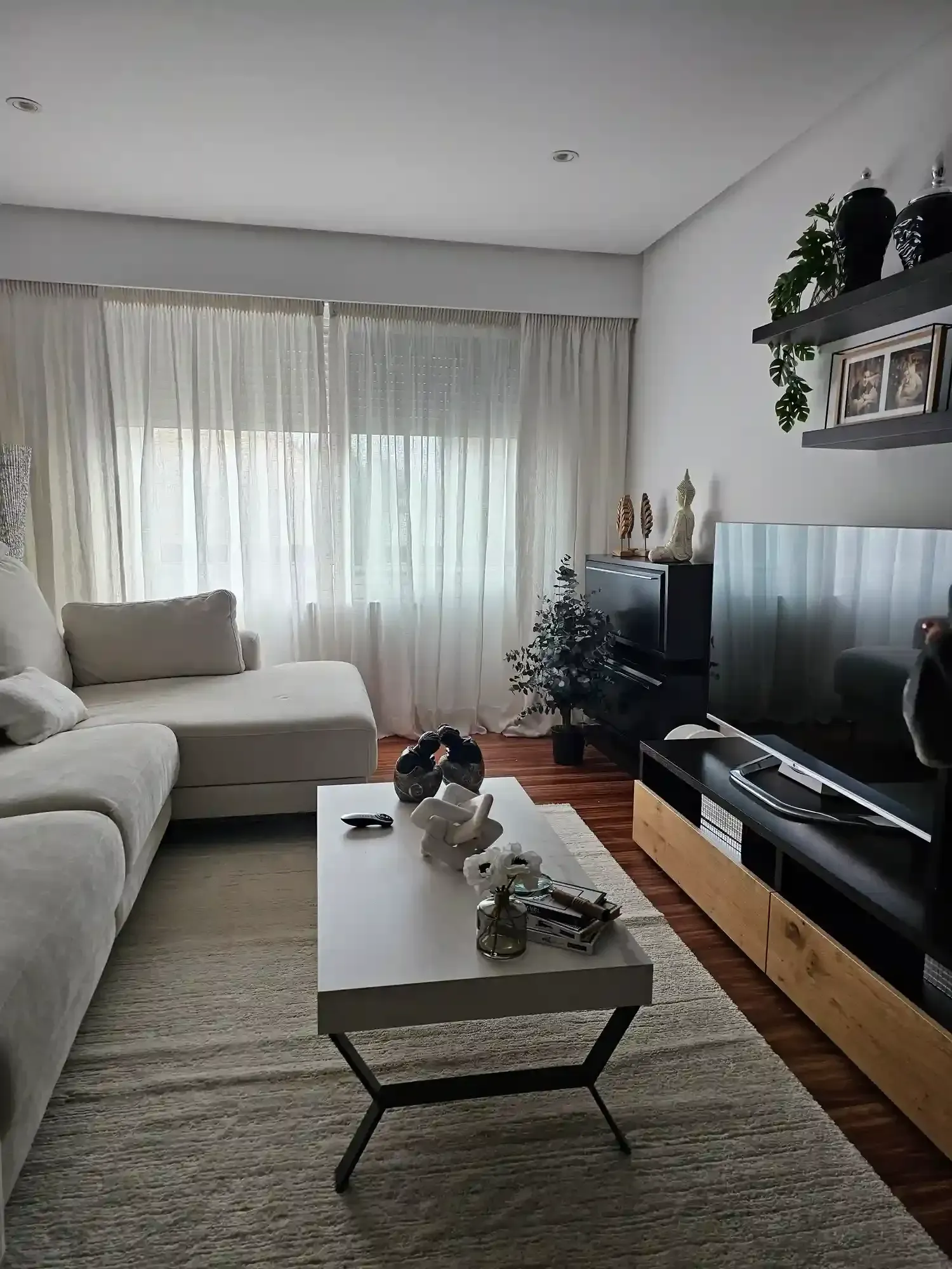 Luminoso salón con sofá modular, mesa de centro, televisor y cortinas transparentes junto a la ventana.