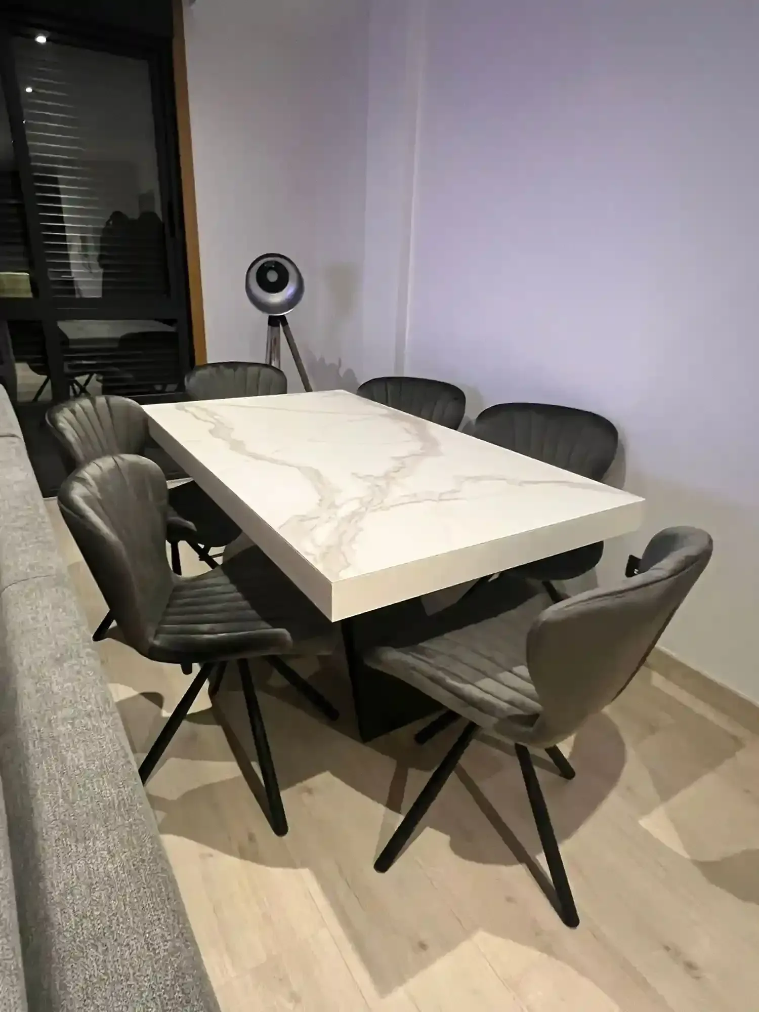Pequeña sala de reuniones con una mesa blanca, sillas negras y una cámara con trípode cerca de una ventana.