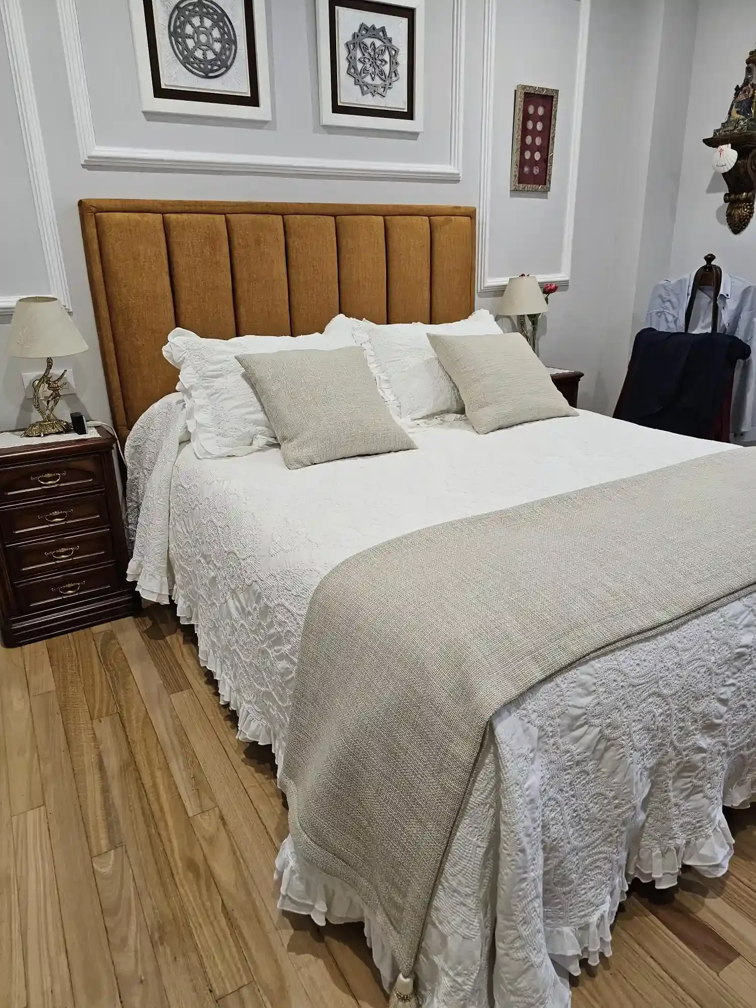 Acogedora habitación con cabecero capitoné beige, ropa de cama blanca y suelo de madera.