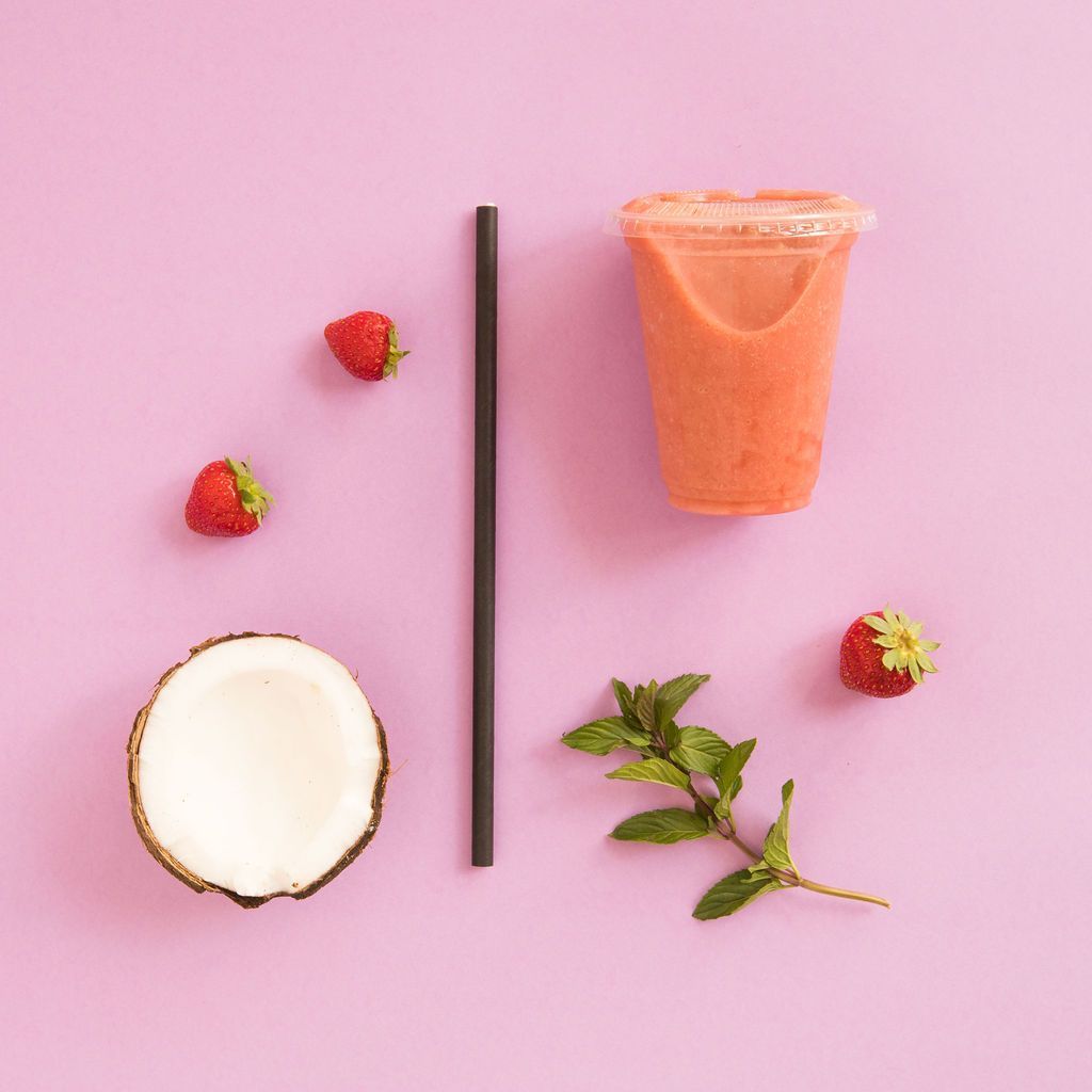 Fresas, coco, menta y una taza de batido sobre un fondo rosa.