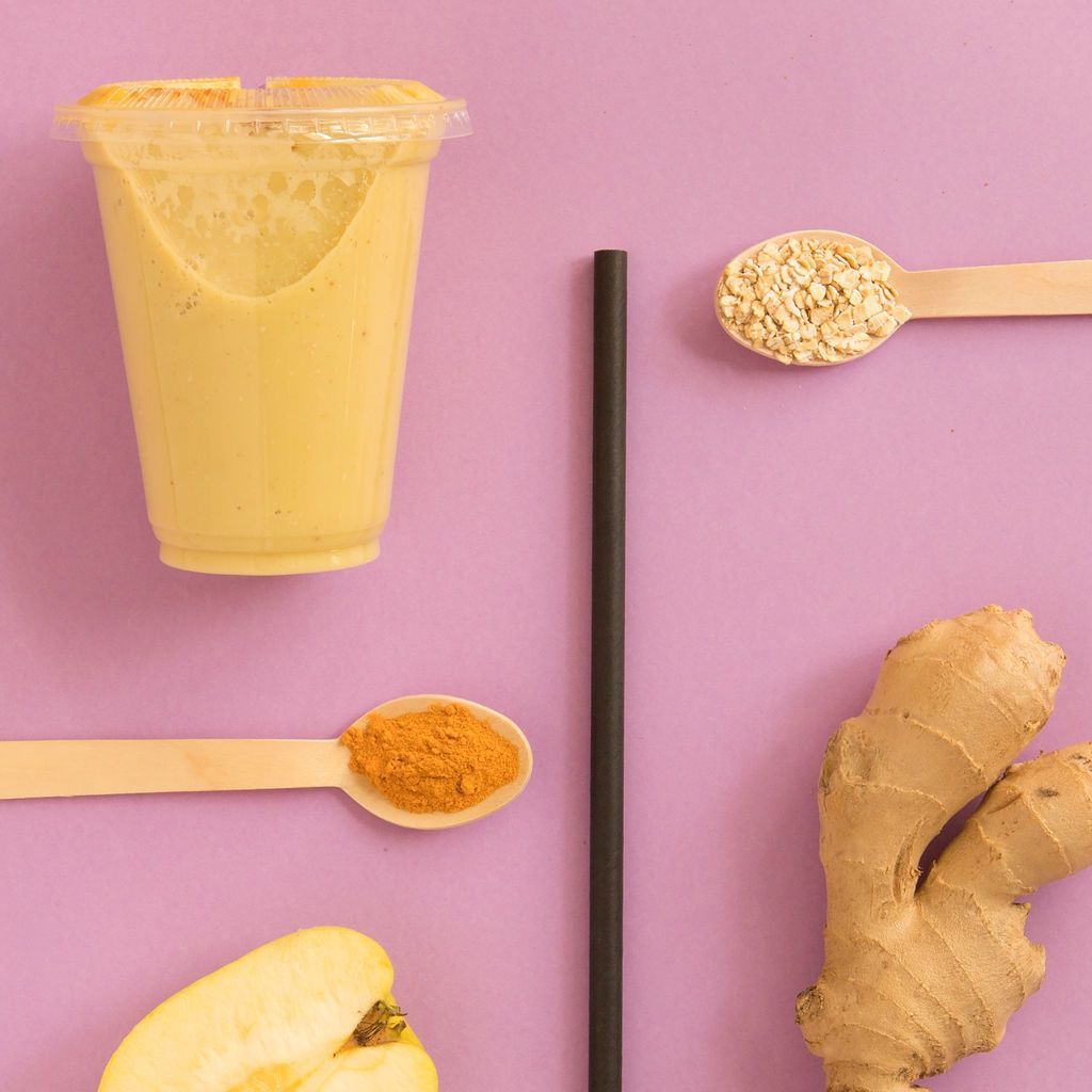 Una taza de batido junto a una cucharada de cúrcuma y jengibre