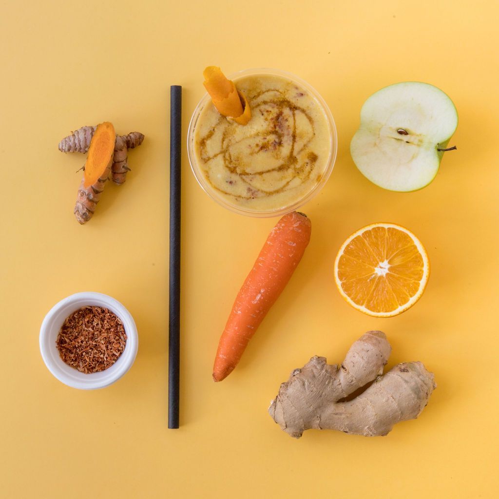 Un batido con zanahorias, manzanas, naranjas, jengibre y cúrcuma sobre un fondo amarillo.