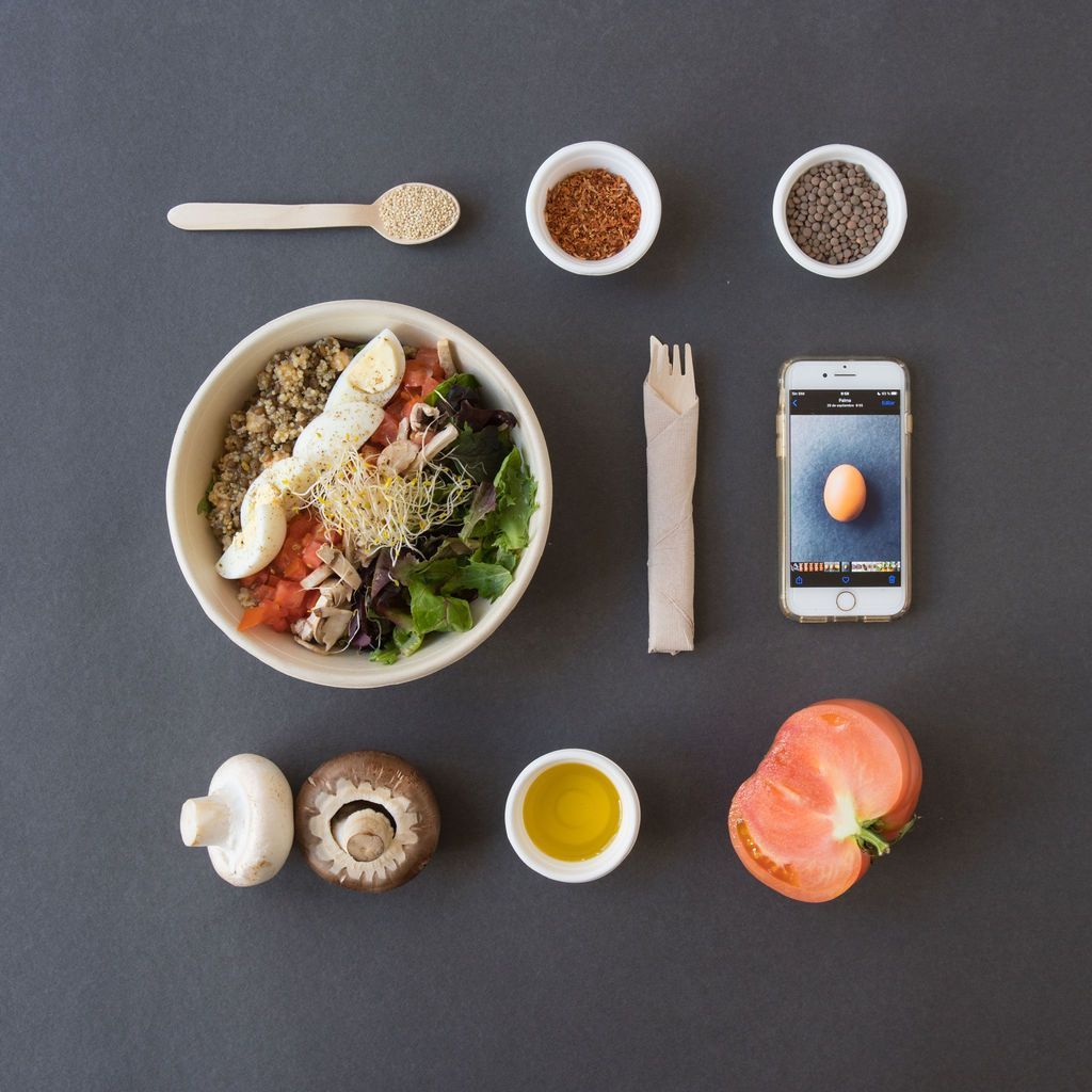 Un plato de comida rodeado de verduras y un teléfono móvil.