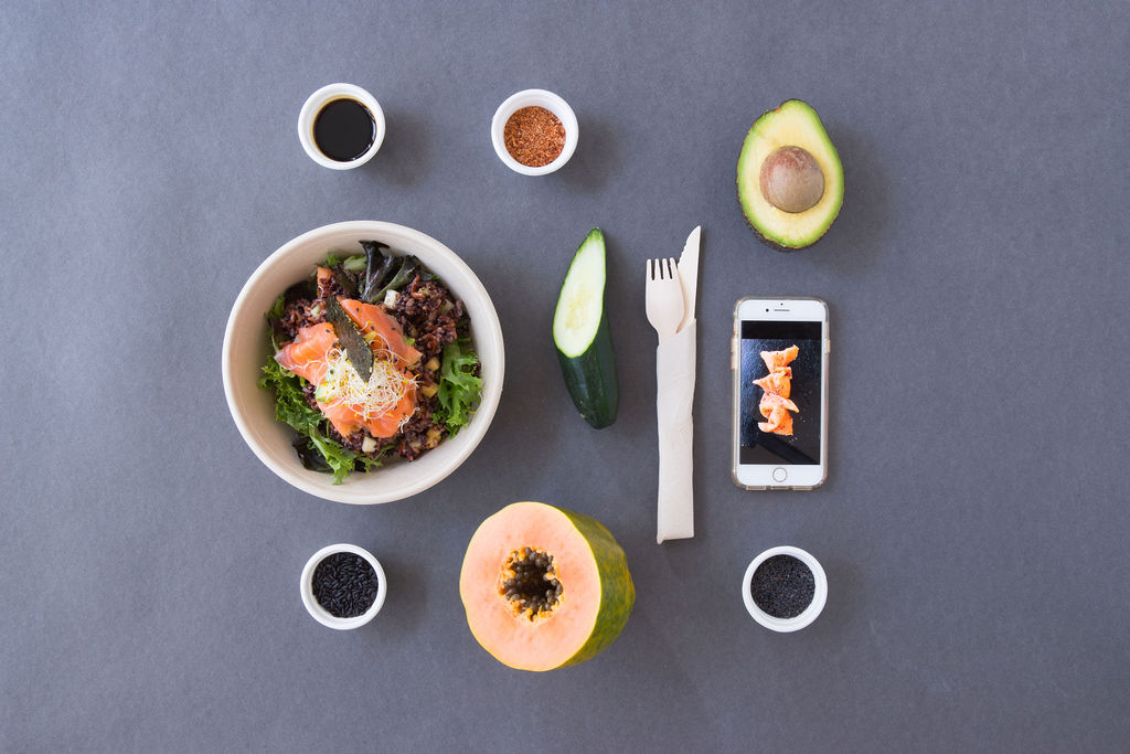 Un plato de comida rodeado de frutas y verduras y un teléfono móvil.