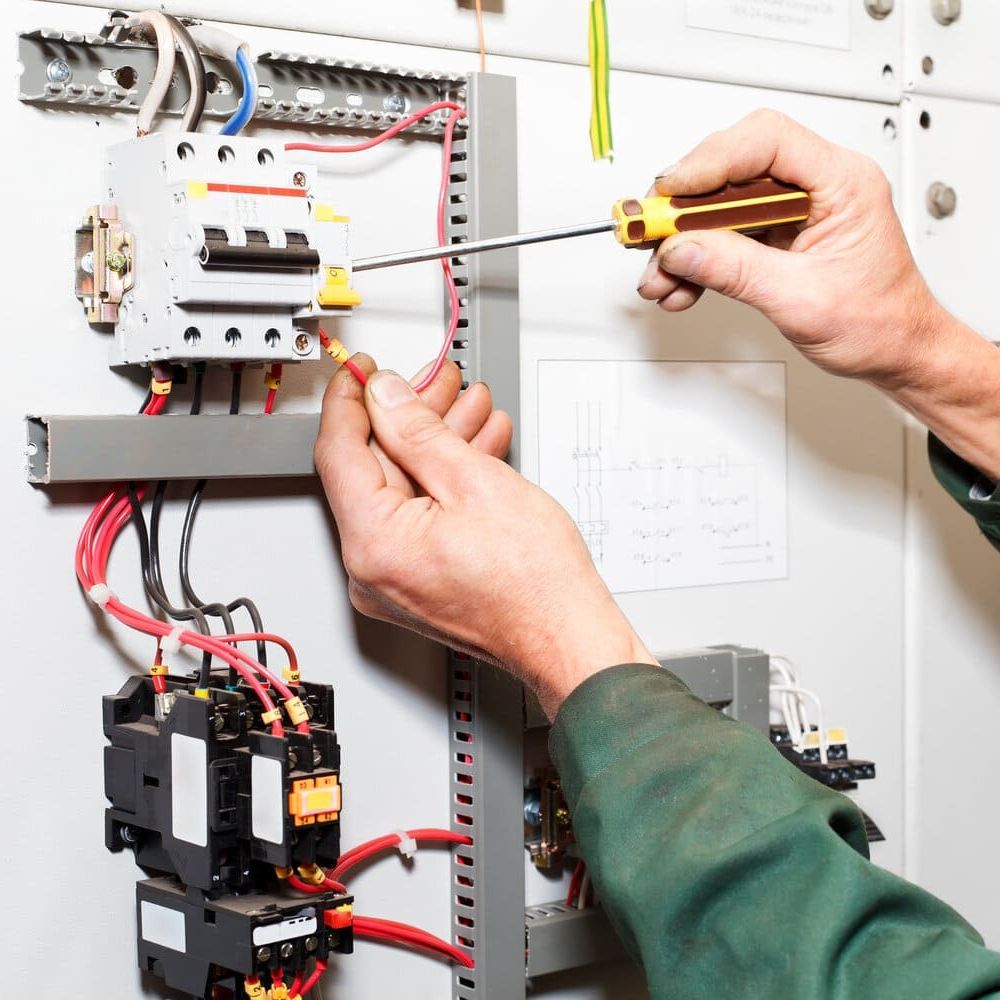 Un hombre está trabajando en una caja eléctrica con un destornillador.