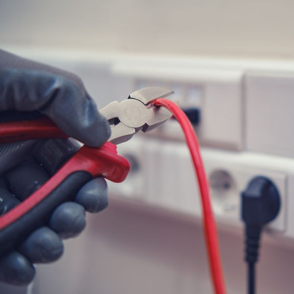 Una persona sostiene un par de alicates sobre un cable rojo.