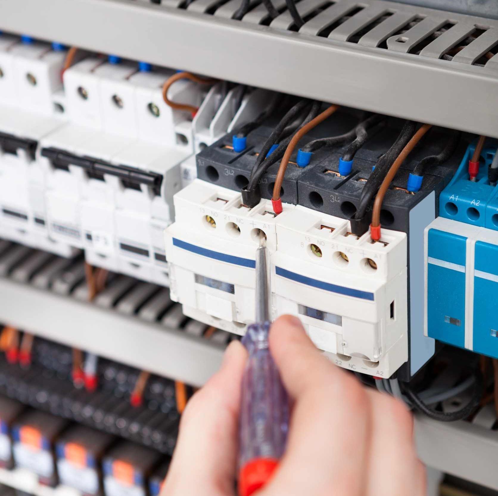Una persona está trabajando en un panel eléctrico con un destornillador.