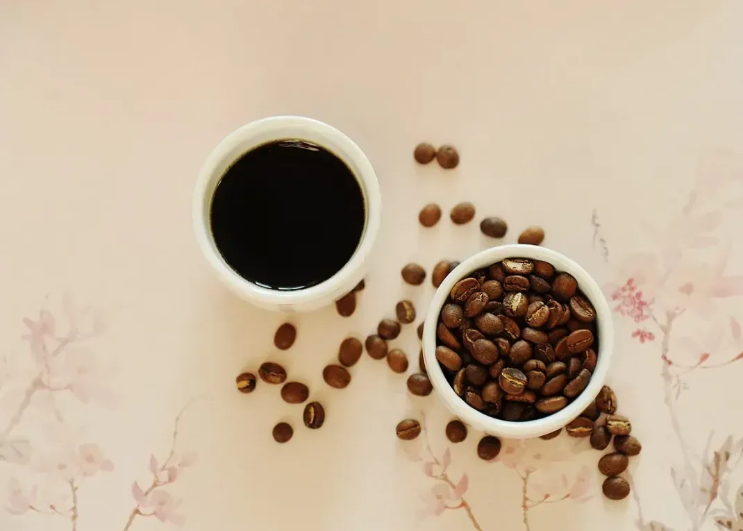 Dos tazas de café y dos tazones de granos de café sobre una mesa.