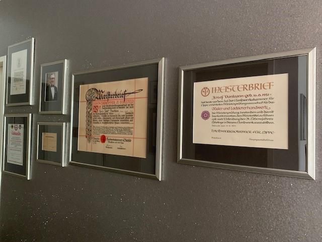 Eine Reihe gerahmter Papiere an einer Wand, eines davon ist ein Diplom