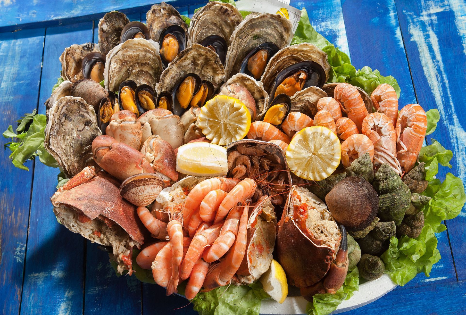 Plateau de fruits de mer assortis avec moules, crevettes, huîtres, tranches de citron et salade verte sur un plateau bleu