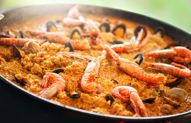 Paella aux fruits de mer dans une grande poêle, garnie de crevettes et de moules, fumante