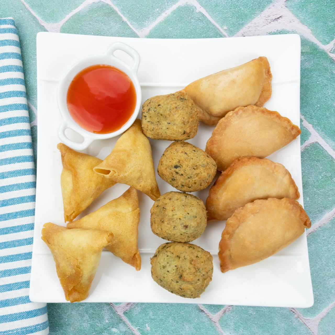 Assiette blanche garnie d'un assortiment de beignets, comprenant des samoussas, des croquettes et une sauce rouge.