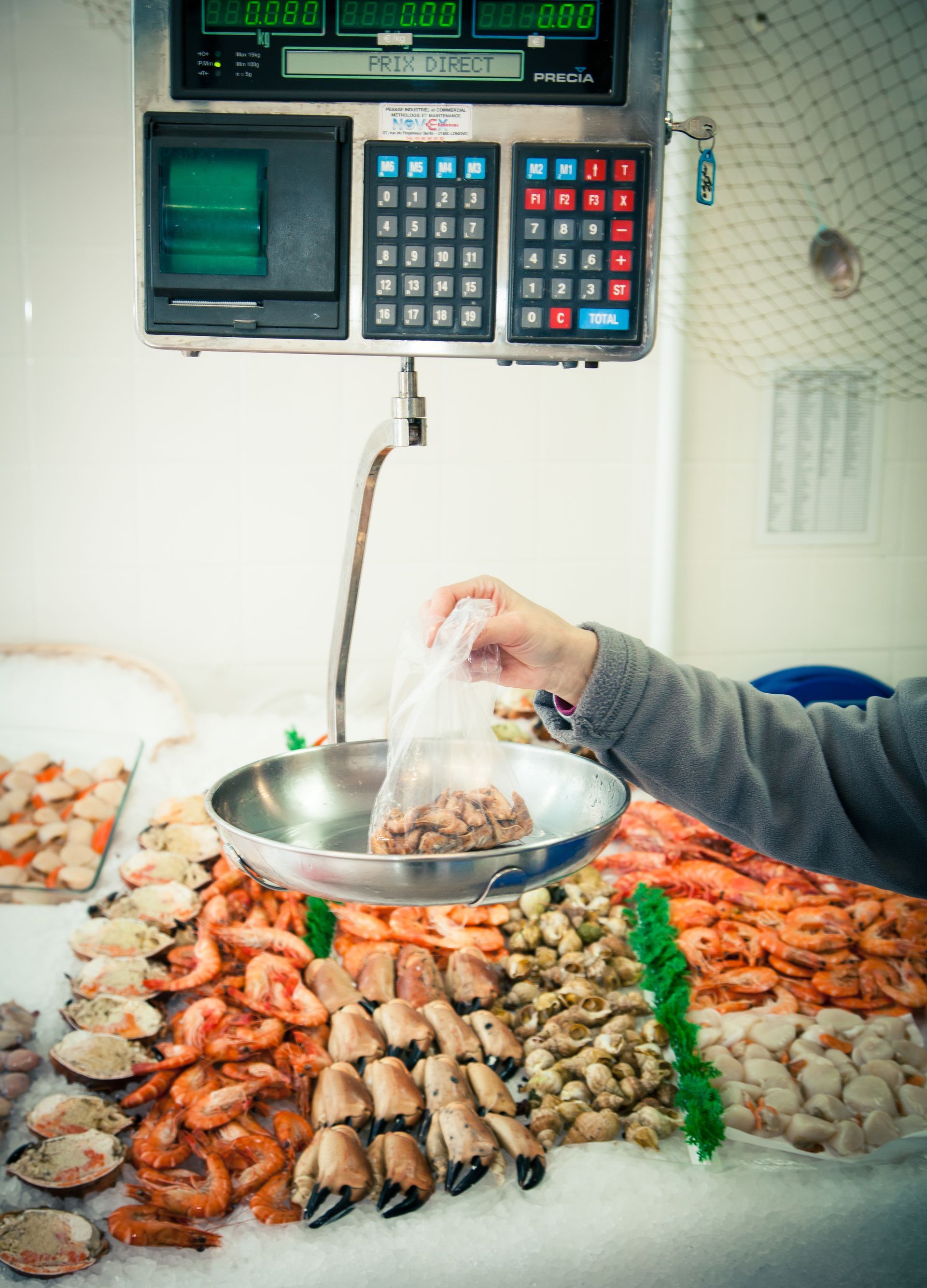 Un vendeur déposant les fruits de mer dans un bol en métal à côté d'une balance numérique.
