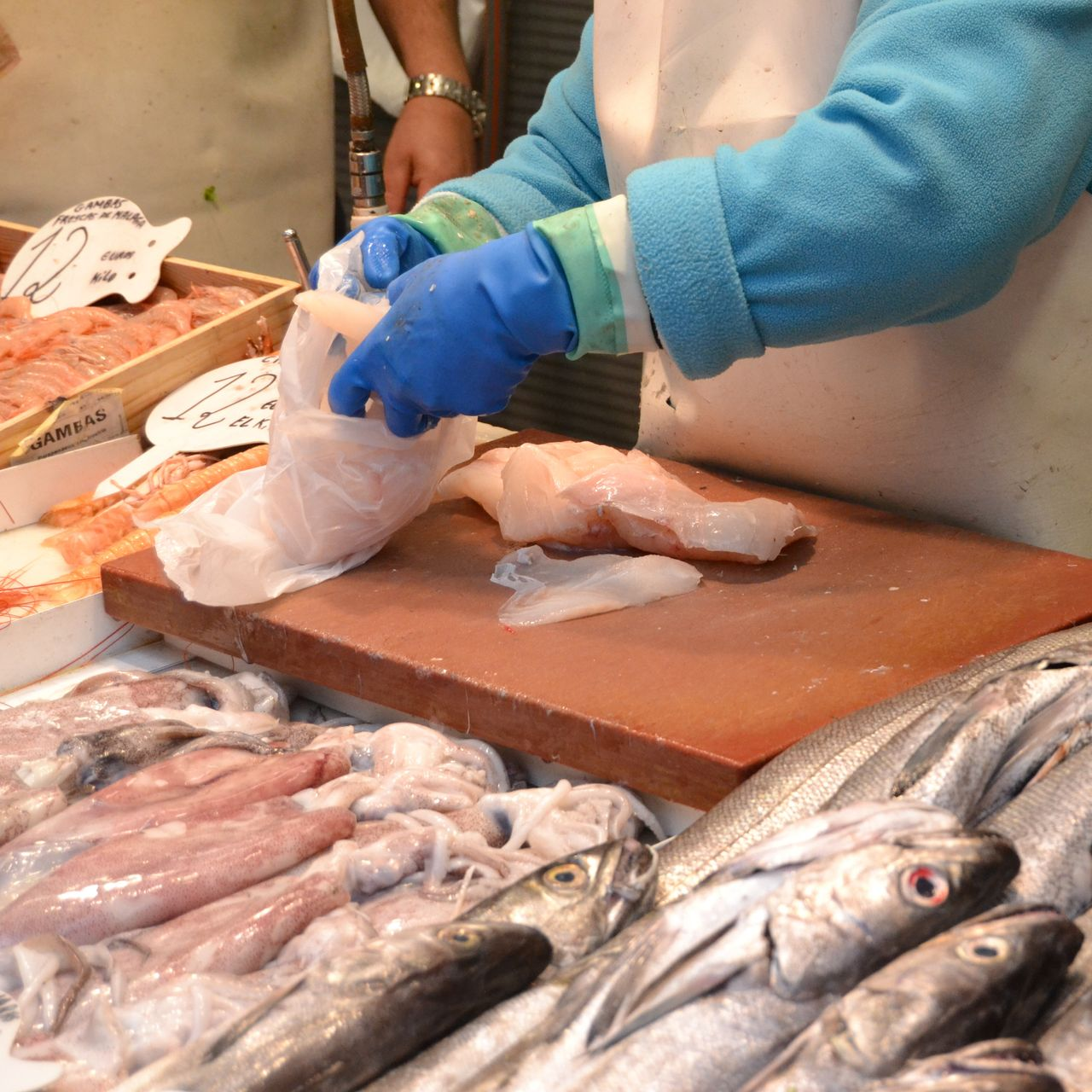 Un vendeur portant des gants bleus emballe du poisson sur un étal de marché