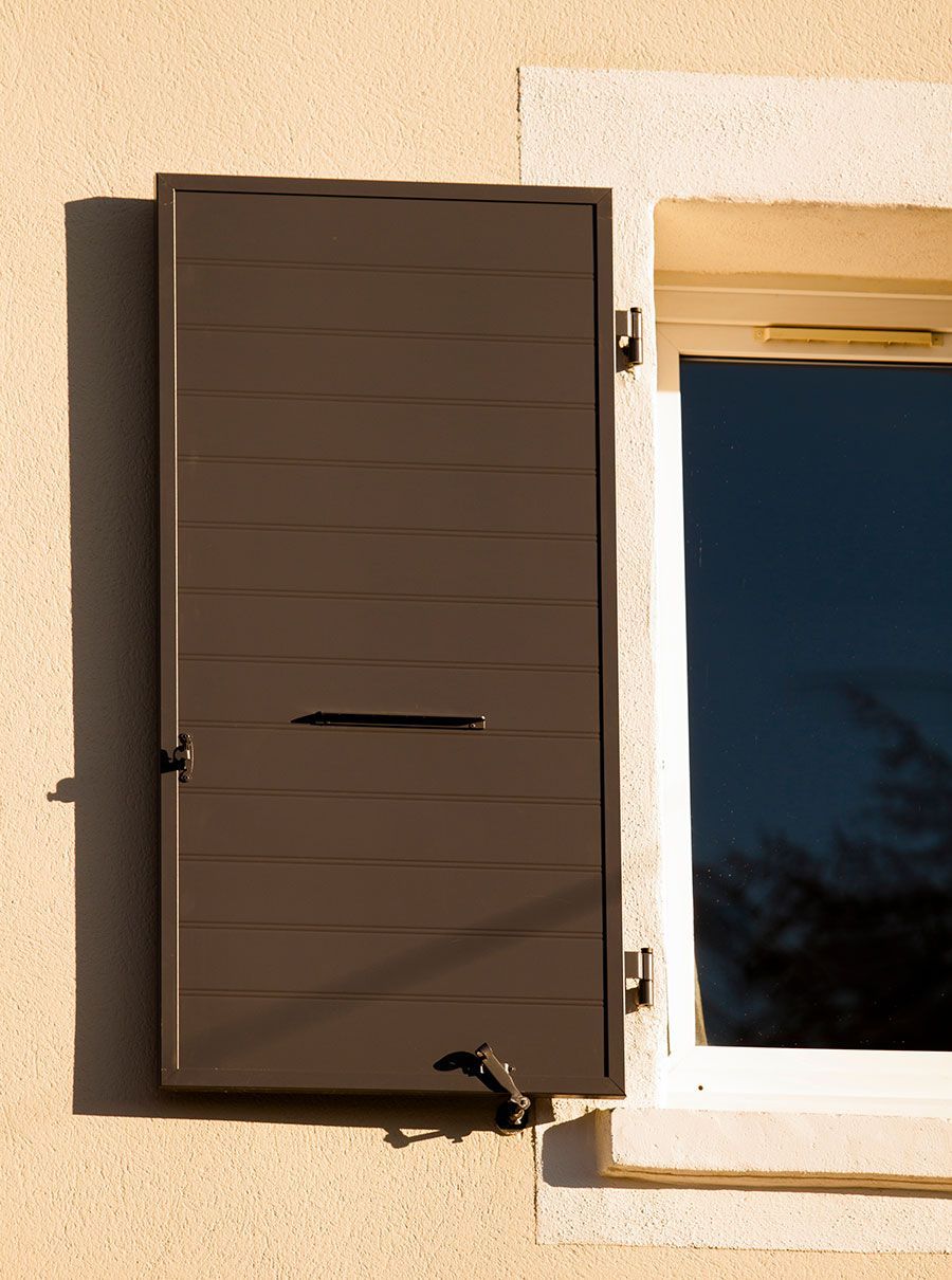 Volet marron à côté d'une fenêtre sur l'extérieur d'un bâtiment de couleur claire.