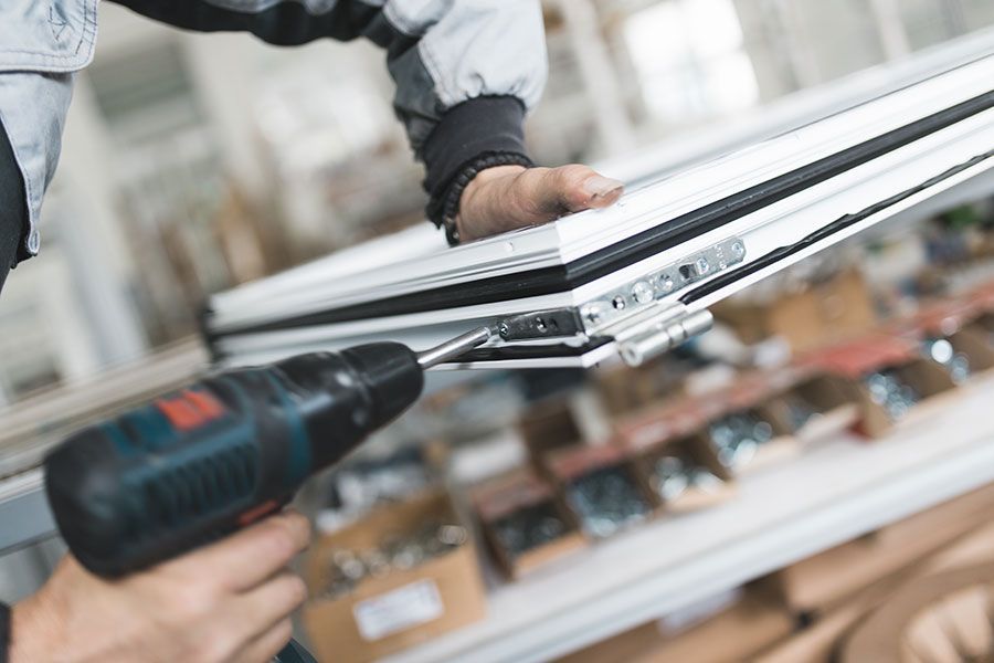 Personne utilisant une perceuse électrique pour assembler un cadre de fenêtre blanc dans un atelier.