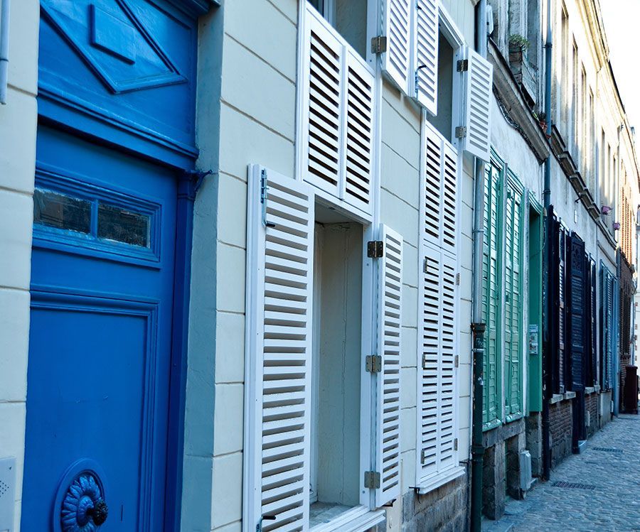 Porte bleue et rangée de bâtiments aux volets blancs et colorés.
