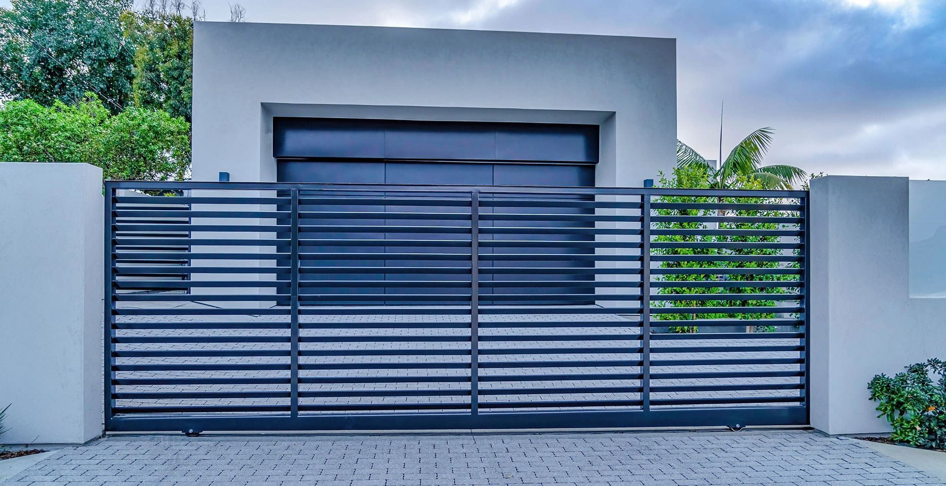 Portail en métal gris devant un bâtiment blanc moderne avec fenêtre sombre.