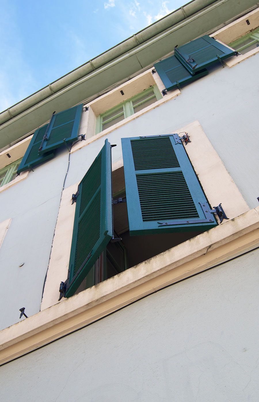 Extérieur du bâtiment avec des volets bleus sur des fenêtres ouvertes, sur fond de façade bleu clair.
