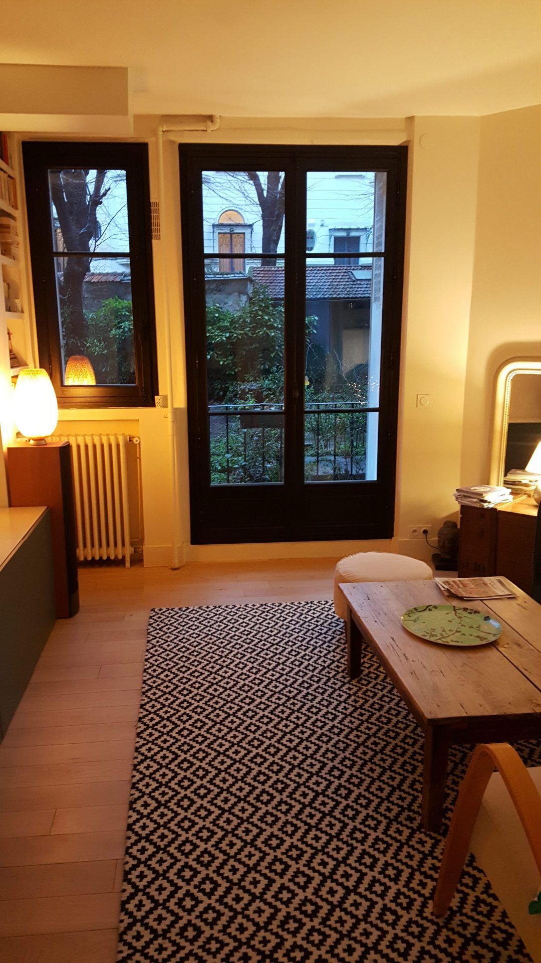 Séjour avec parquet, tapis noir et blanc et porte donnant sur un jardin.