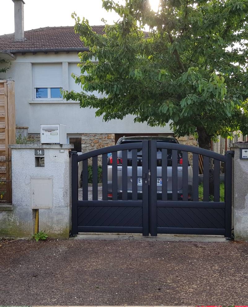 Portail noir devant une maison claire. Une voiture est visible derrière le portail.