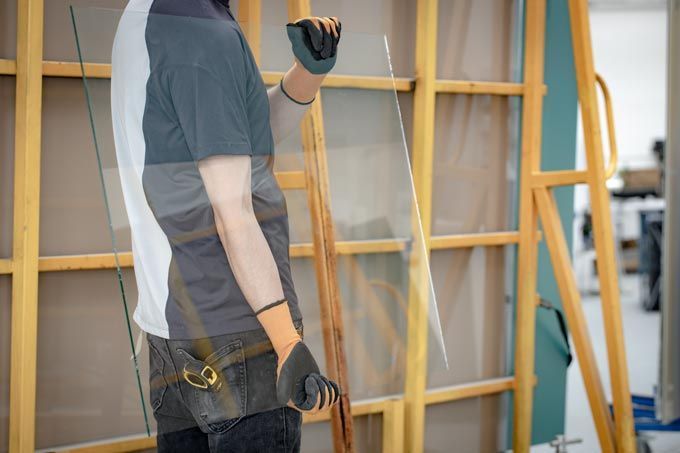 Une personne portant des gants tient une grande vitre près d'un cadre en bois dans un atelier.