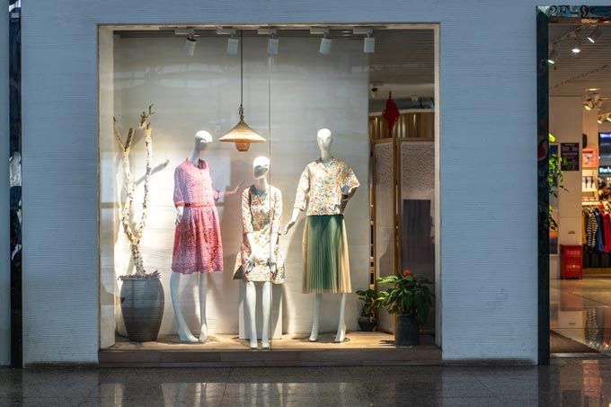 Vitrine d'un magasin de vêtements avec trois mannequins portant des robes et des jupes.