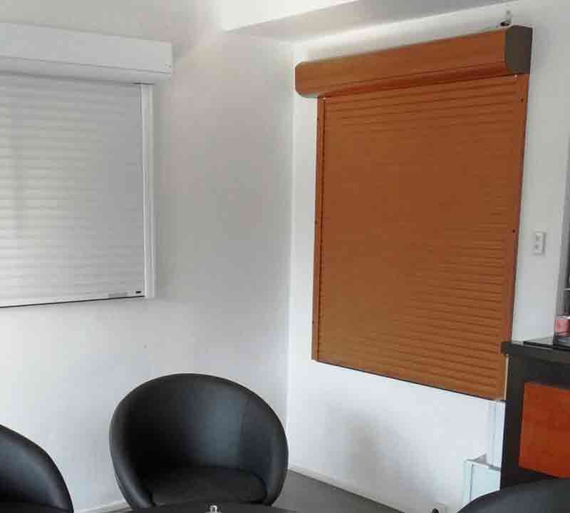 Vue intérieure : Deux fenêtres avec stores fermés, une blanche et une marron, au dessus de chaises noires.