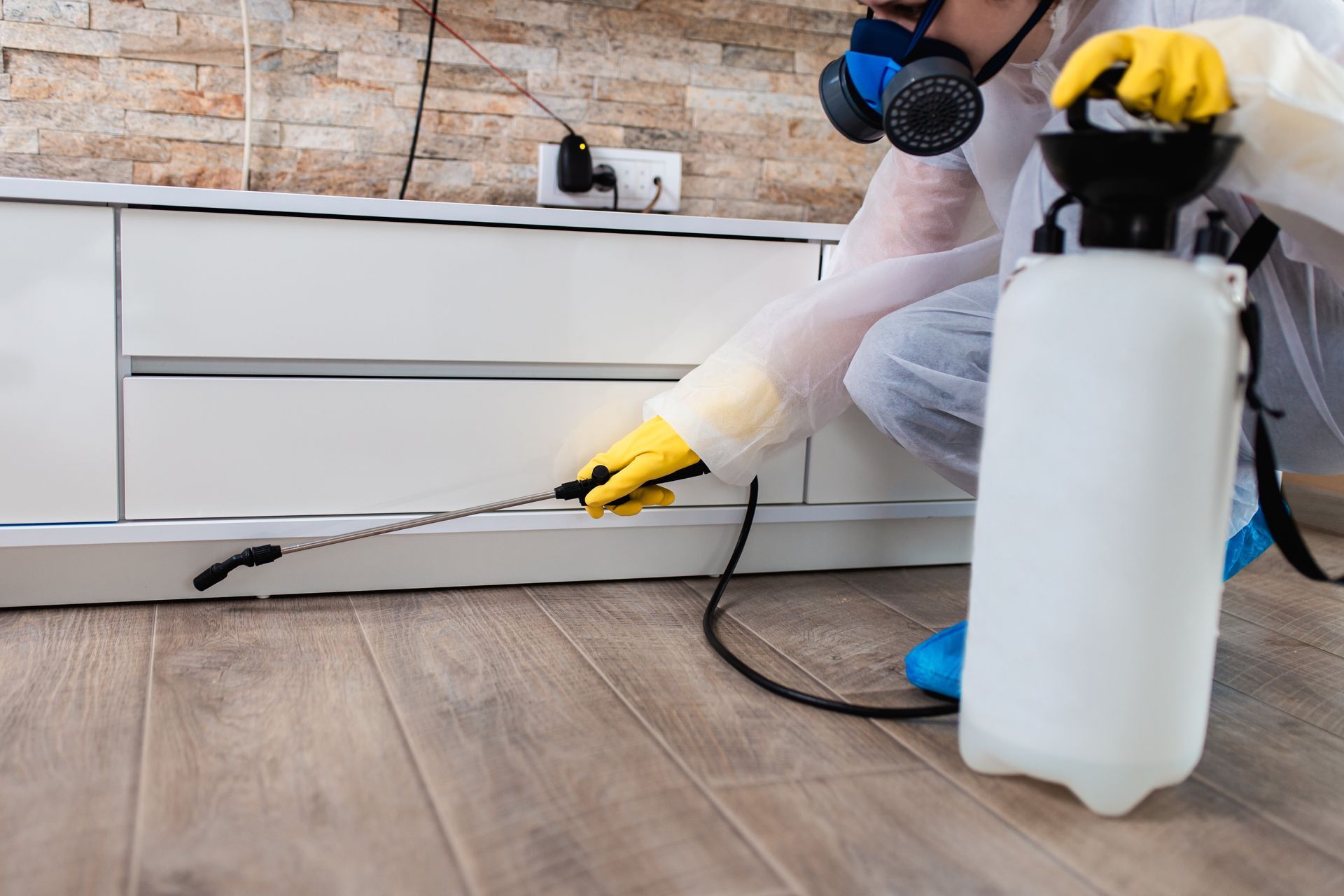 Une personne portant un équipement de protection pulvérise du désinfectant le long d'une plinthe dans une pièce