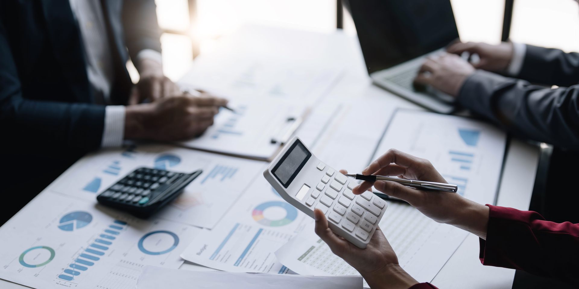 Personas revisando gráficos financieros y una calculadora durante una reunión de negocios.