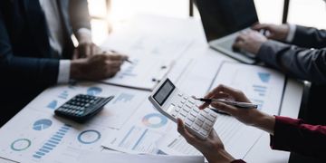 Personas revisando gráficos financieros y una calculadora durante una reunión de negocios.