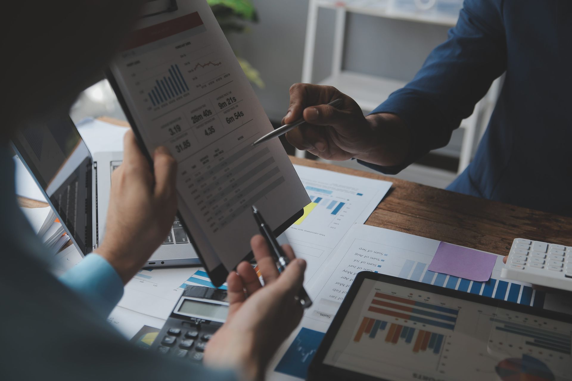 Personas revisando gráficos impresos y tablas financieras en un escritorio con una computadora portátil y una tableta.