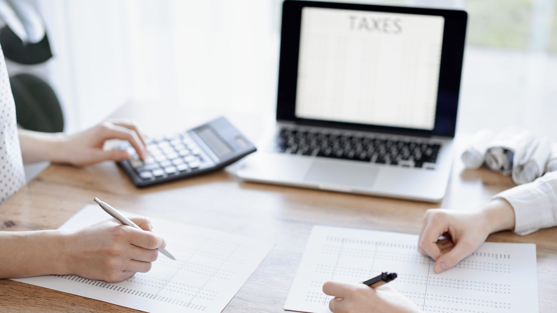 Personas revisando formularios de impuestos en un escritorio con una computadora portátil etiquetada como 