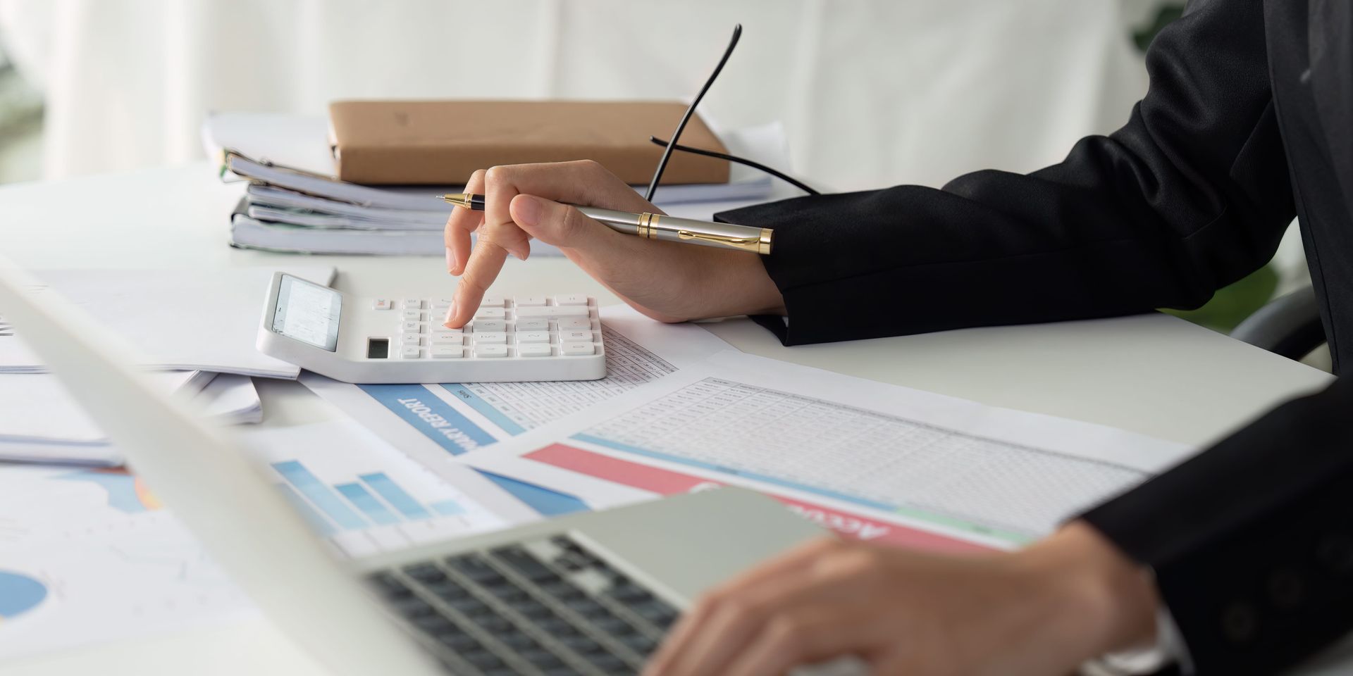 Manos revisando gráficos y documentos en un escritorio con calculadora y bolígrafo.