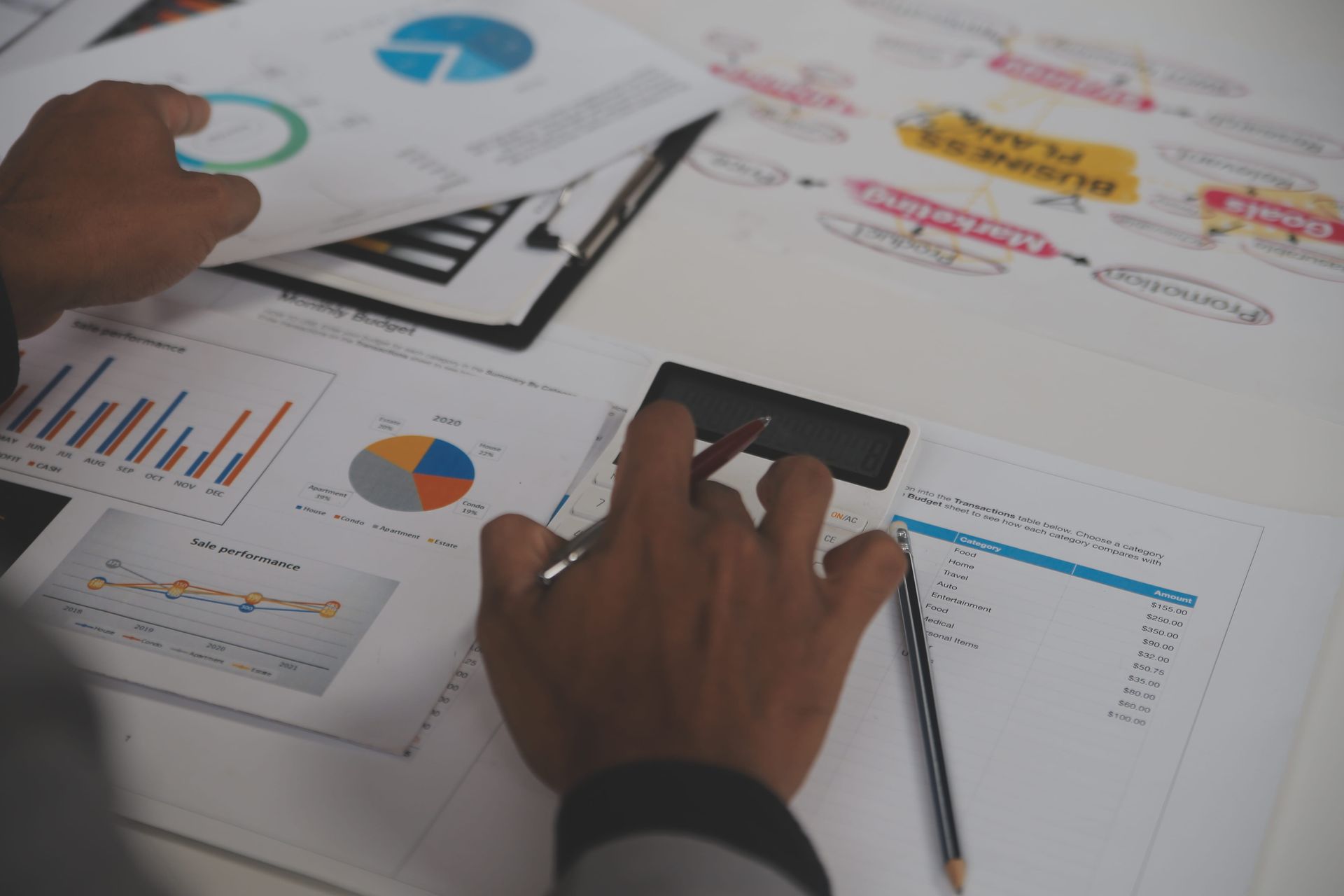 Manos revisando gráficos y tablas impresas sobre un escritorio durante una reunión de negocios.