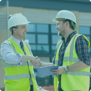 Two men wearing hard hats and safety vests are shaking hands.