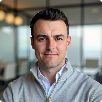 Man in gray sweater and white shirt, looking at the camera, office setting.