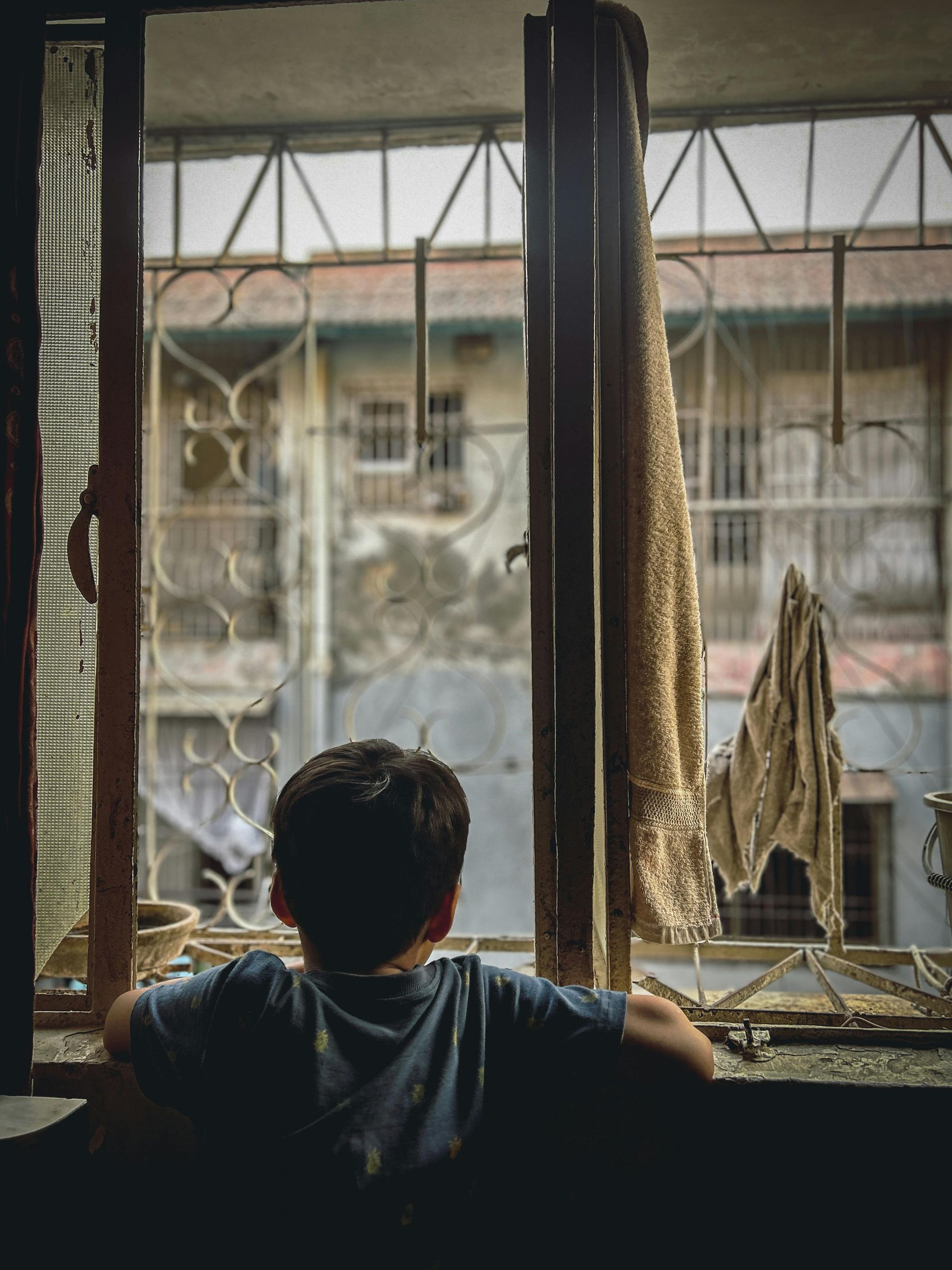 A boy in a blue shirt is looking out of a window
