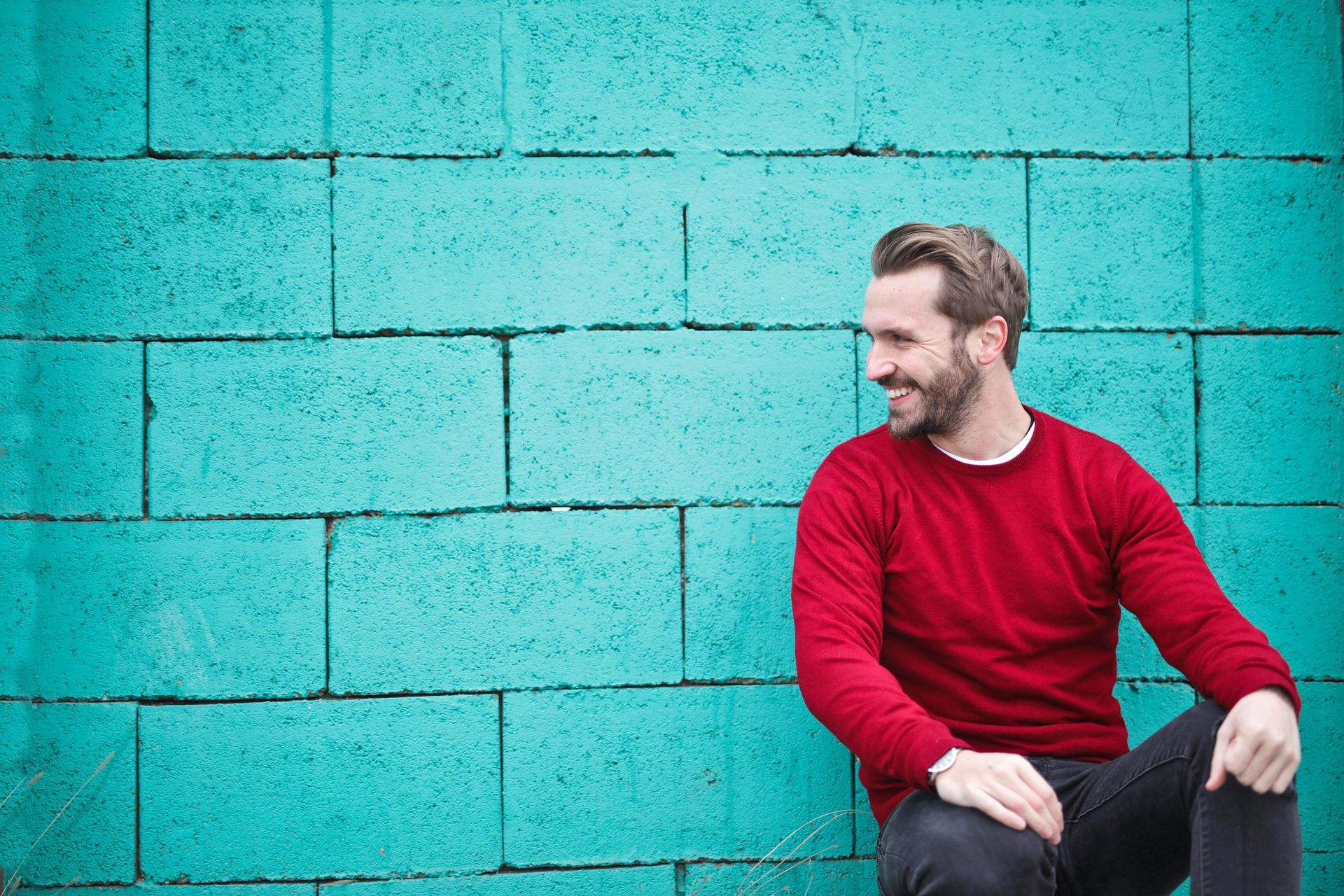A man in a red sweater is sitting in front of a blue brick wall.