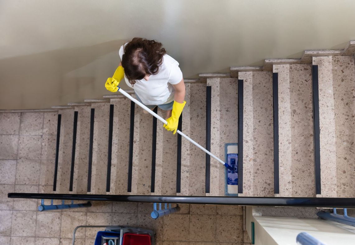 Pessoa limpando uma escada, usando luvas amarelas, vista de cima.